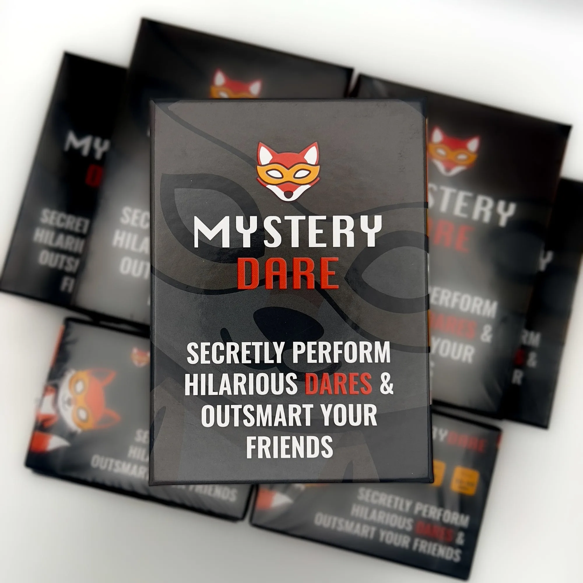 The Mystery Dare box propped upright in front of several more copies, reading 'Secretly perform hilarious dares & outsmart your friends'